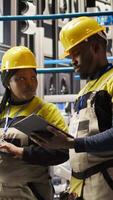 Vertical Team of smart factory mechanics working together to test systems, doing maintenance. Industry 4.0 plant teamworking repairmen inspecting equipment to identify glitches, doing brainstorming, camera A video