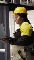 Vertical Smart factory mechanic computerizing operations and monitoring energy consumption using laptop. Repairman walking in industry 4.0 plant with notebook, providing technical support, camera A video