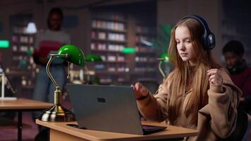 Girl studying in the library to obtain her diploma with focus music on headset, using the academic database for research. Student generating creative ideas for the bachelor paper. Camera A. video