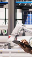 Vertical Smart manufacturing factory engineer using tablet app to calibrate high tech machinery and analyze sensor data. Engineer using digital device to troubleshoot photovoltaic assembly equipment, camera A video