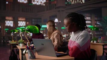 University student making exam preparations with a friend at the campus library, doing research to complete handwritten class notes. Girls sharing information from the database. Camera B. video