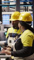 Vertical Engineering team using PC in smart factory to oversee robotic assembly lines, ensuring quality control during manufacturing. Teamworking colleagues monitor automated conveyor belts, camera A video