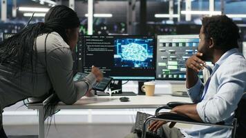 Admin in wheelchair and data center coworker working together using AI node tree software to minimize downtime. Server hub IT expert in disability and colleague using visual programming app, camera B video