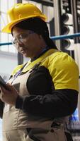 Vertical Smart factory engineer using tablet to analyze IoT sensors data, refining equipment operational efficiency. Industrial plant worker performs system diagnostics to reduce production downtime, camera A video
