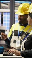 Vertical Engineering team using PC in smart factory to oversee robotic assembly lines, ensuring quality control during manufacturing. Teamworking colleagues monitor automated conveyor belts, camera B video