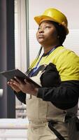 Vertical Engineer walks in photovoltaics factory, looking at system performance metrics on tablet. Worker administrates industry 4.0 plant, using device to track energy production through IoT sensors, camera A video