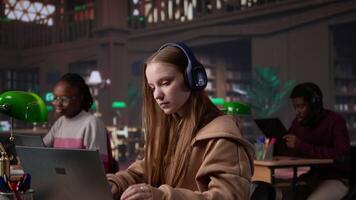 Young student attending to a web lecture with headset in the campus library, takes notes and learns about politics in an online meeting. Focused pupil during class lesson. Camera B. video