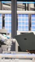 Vertical Technician in solar panels factory oversees robot assembly lines using laptop, ensuring quality control. Industrial plant worker monitoring automated conveyor systems using notebook, camera B video