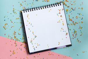 Top view of open notebook with clean sheet on bright vivid blue, pink, background with colorful confetti .Template for message. photo