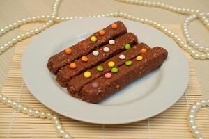 On a smooth, light wooden surface, a white round plate holds several chocolate coated snack bars photo