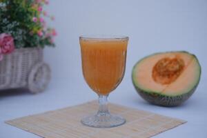 a refreshing glass of cantaloupe juice placed at the center, served in an elegant glass with a textured design photo