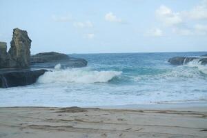 Just beyond the shore, waves crash energetically against the rocky formations jutting out from the sea photo