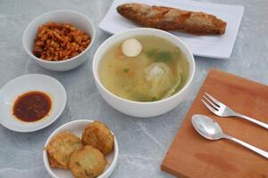 At the center is a bowl of clear soup containing vegetables, a fish ball, and possibly dumplings or cabbage. photo