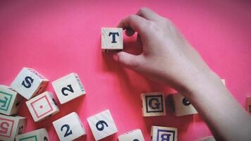 A small child hand is seen holding a wooden block labeled with the letter T. Child learning concept isolated on red background photo