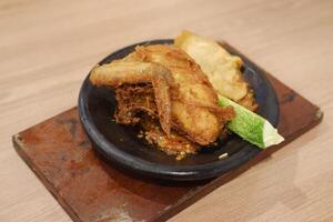 The dish features a piece of crispy fried chicken served on a traditional stone plate. It sits atop a spicy sambal chili sauce, adding a vibrant and flavorful base photo