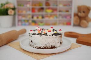 The cake is coated with a layer of whipped cream, lightly covering the chocolate sponge beneath photo
