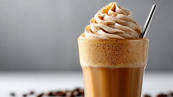 A clear glass cup filled with a creamy iced cappuccino, topped with a generous swirl of frothy milk and a straw inserted at a slight angle photo