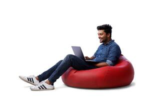 An Asian fashion model is sitting on a bean bag and working on his laptop. photo