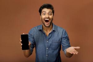 With a surprised expression, handsome young model is showing the screen of his smartphone. photo
