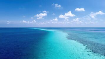 Tropical ocean horizon with clear blue water under a bright sky with fluffy clouds and a visible coral reef below the surface. photo