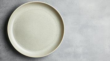 Minimal Beige Ceramic Plate On Gray Surface with speckled texture and soft lighting ideal for food styling or tableware design mockups. photo