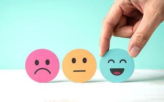 A person holding a smiley face on a piece of paper with three different colored smiley faces photo