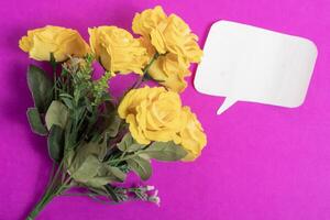Bouquet of yellow roses with a blank speech bubble on a bright pink background. photo