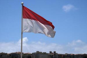 The flag of Monaco in the wind in front of a blue sky photo