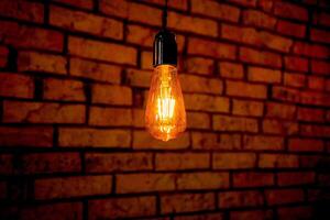 Old electric incandescent lamp with tungsten filament. Against the backdrop of a brick wall. Texture of old stone background. photo