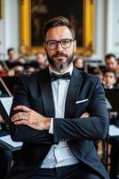 A man in a tuxedo and bow tie standing in front of an orchestra photo
