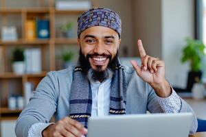 A man sitting at a table with a laptop and pointing up photo