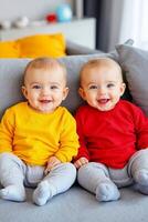 Two babies sitting on a couch smiling at the camera photo