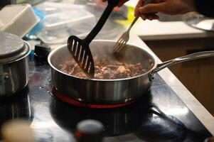 Hand using kitchen flipper frying sliced beef in pan photo