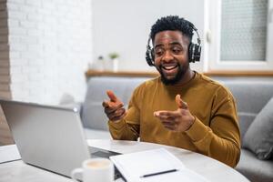 Happy African American man having a call at home, using a laptop and wireless technology for remote communication. photo