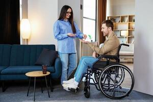 Man in wheelchair extend her hand palm up to side. Woman giving key with keychain from new house for handicapped. photo
