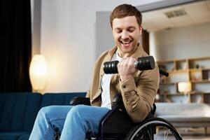 Physical rehabilitation for disabled people. Happy guy in wheelchair making exercises with dumbbell at home. Cheerful impaired young man working out with weights photo