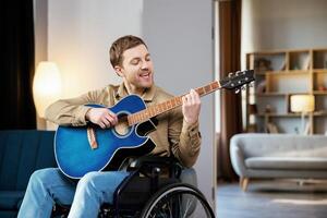 Man with a disability sitting in wheelchair playing on guitar at home. photo