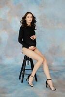 Pregnant model sitting on stool caressing belly. photo