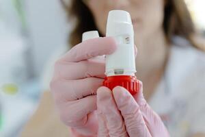 Female doctor holding and showing asthma inhaler. Medical portable equipment for asthma attack photo
