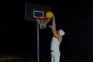 Man performs slam dunk on a basketball court at night under the glare of bright outdoor lights photo