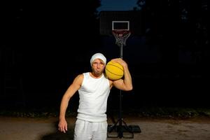 Man holding a basketball in a park at dusk, showcasing athleticism and confidence by the court. photo