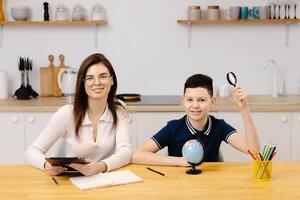 A young woman helps boy with his lessons using a tablet and a globe. A homeschooling student does his homework with the help of a tutor. photo