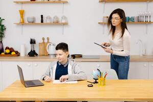 A young woman helps boy with his lessons using a tablet and a globe. A homeschooling student does his homework with the help of a tutor photo