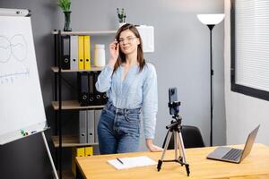 Woman mentor recording presentation, webinar on smartphone standing on tripod, teacher coach explaining, holding online lesson, using phone webcam photo