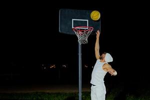 A man performs a slam dunk on a basketball court at night under the glare of bright outdoor lights. photo