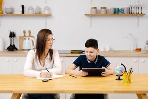 Young woman helps boy with his lessons using a tablet and a globe. A homeschooling student does his homework with the help of a tutor. photo