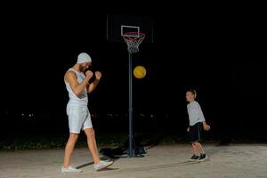 Nighttime basketball game between a child and an adult on an outdoor court under bright lights photo