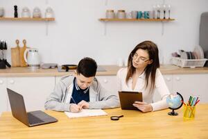 A young woman helps a boy with his lessons using a tablet and a globe. A homeschooling student does his homework with the help of tutor. photo