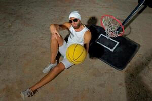 Basketball player sits on the court wearing sunglasses, relaxed after an intense practice session at dusk photo