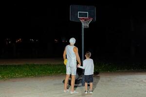 Father and son enjoying a late-night basketball game together at an outdoor court under the stars photo